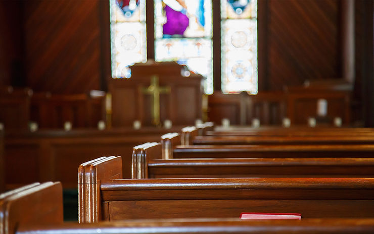 Empty church pews with a red book, stained glass windows in the background, featuring warm wooden tones and a serene atmosphere.